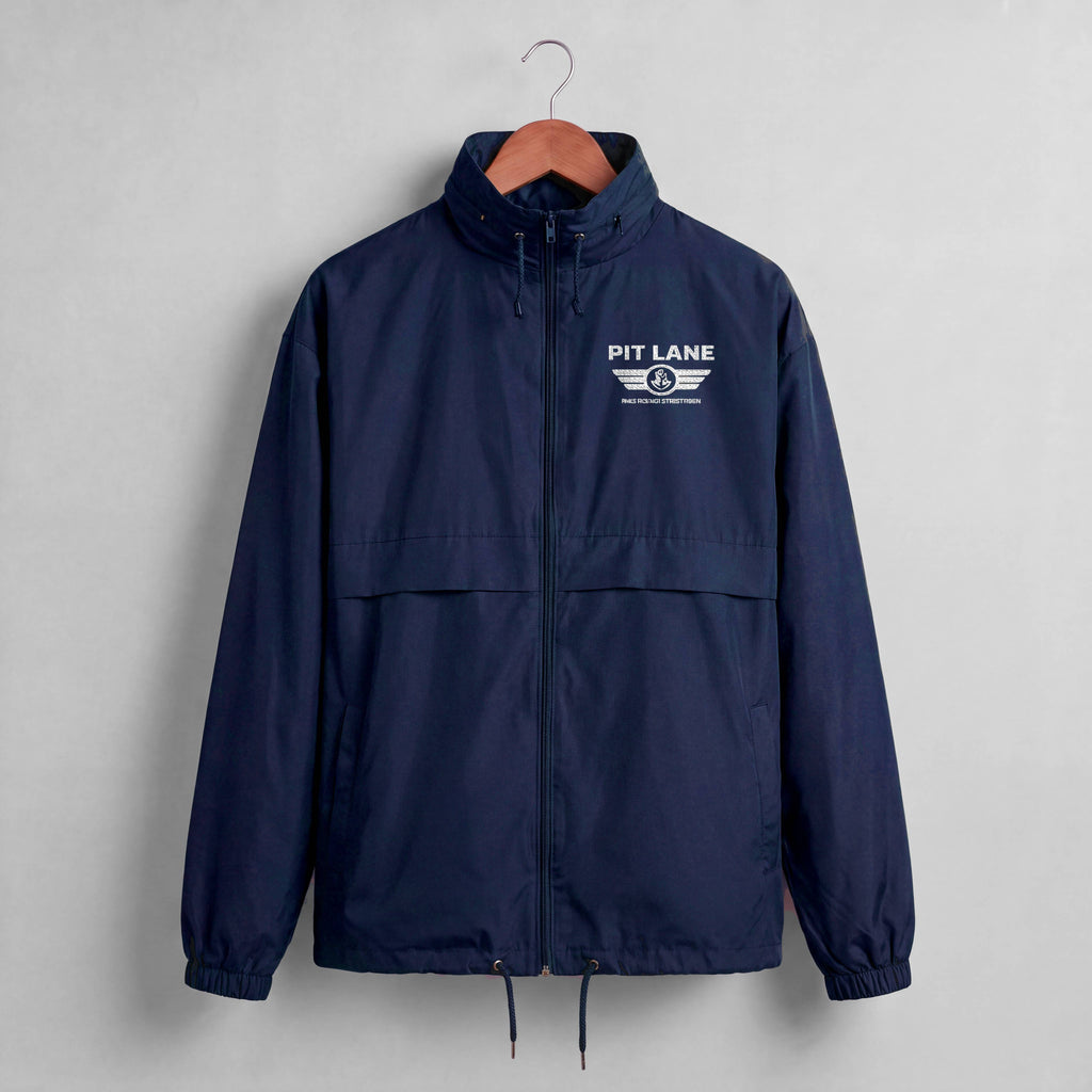 A navy blue windbreaker jacket hanging on a wooden hanger against a light gray wall. The jacket features a white 'PIT LANE' wing logo printed on the left chest.