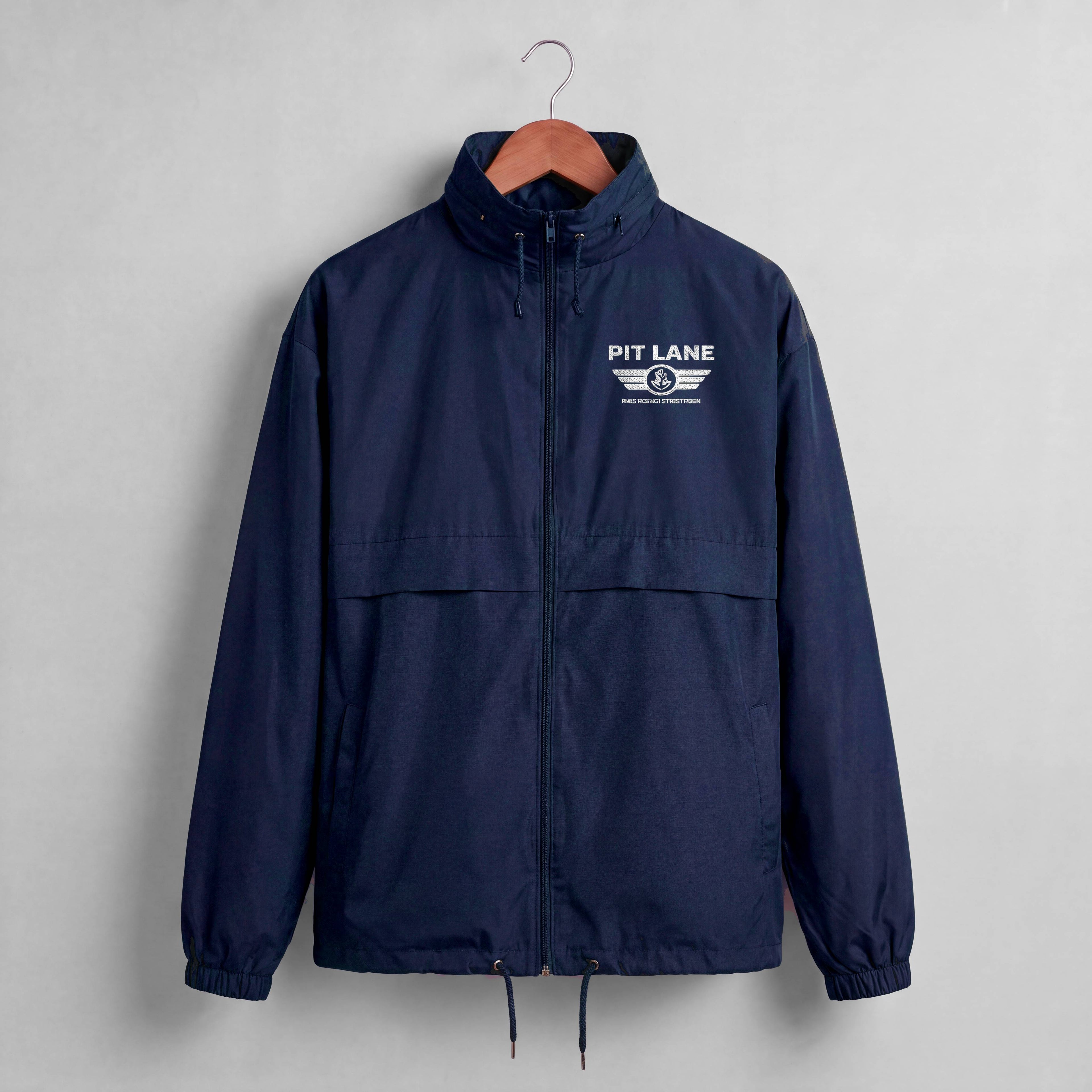 A navy blue windbreaker jacket hanging on a wooden hanger against a light gray wall. The jacket features a white 'PIT LANE' wing logo printed on the left chest.