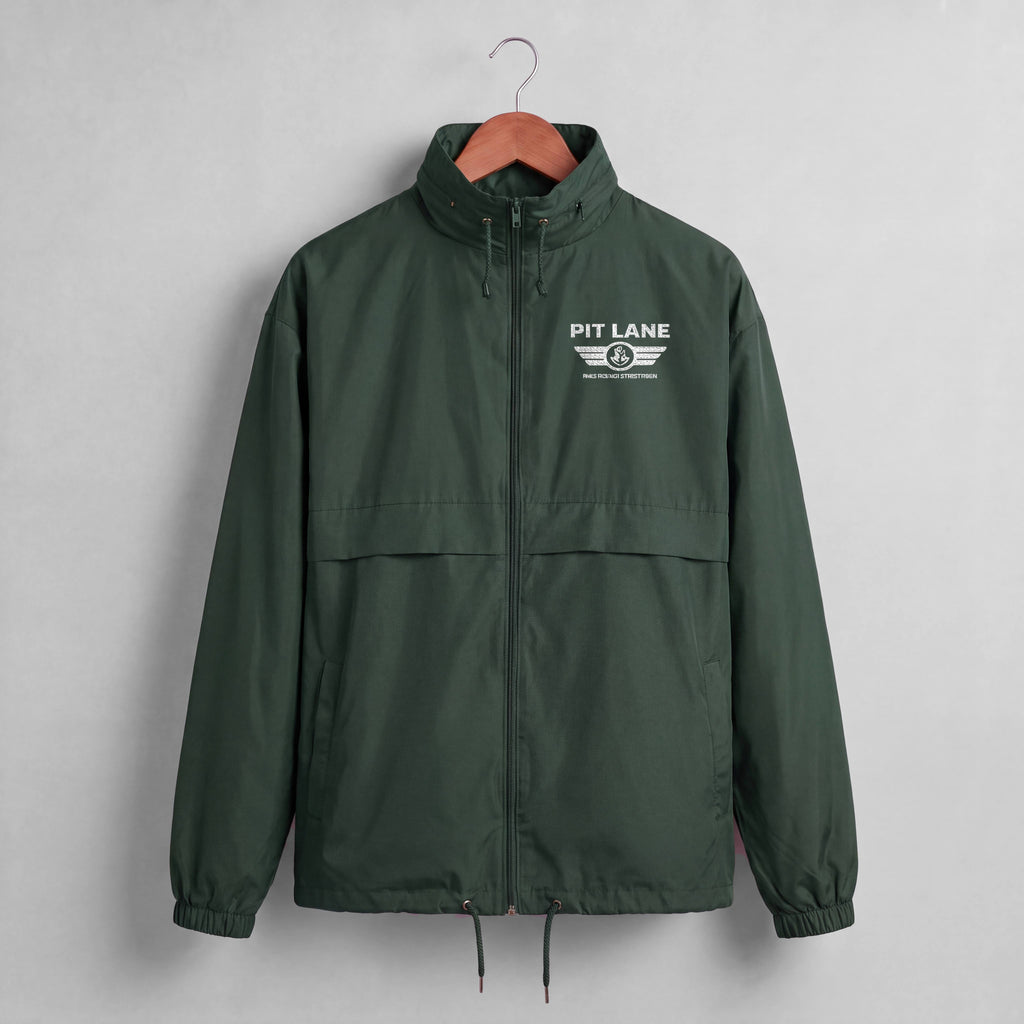 A dark green hooded windbreaker jacket hanging on a wooden hanger against a light gray wall. The jacket features a white 'PIT LANE' winged logo printed on the left chest.
