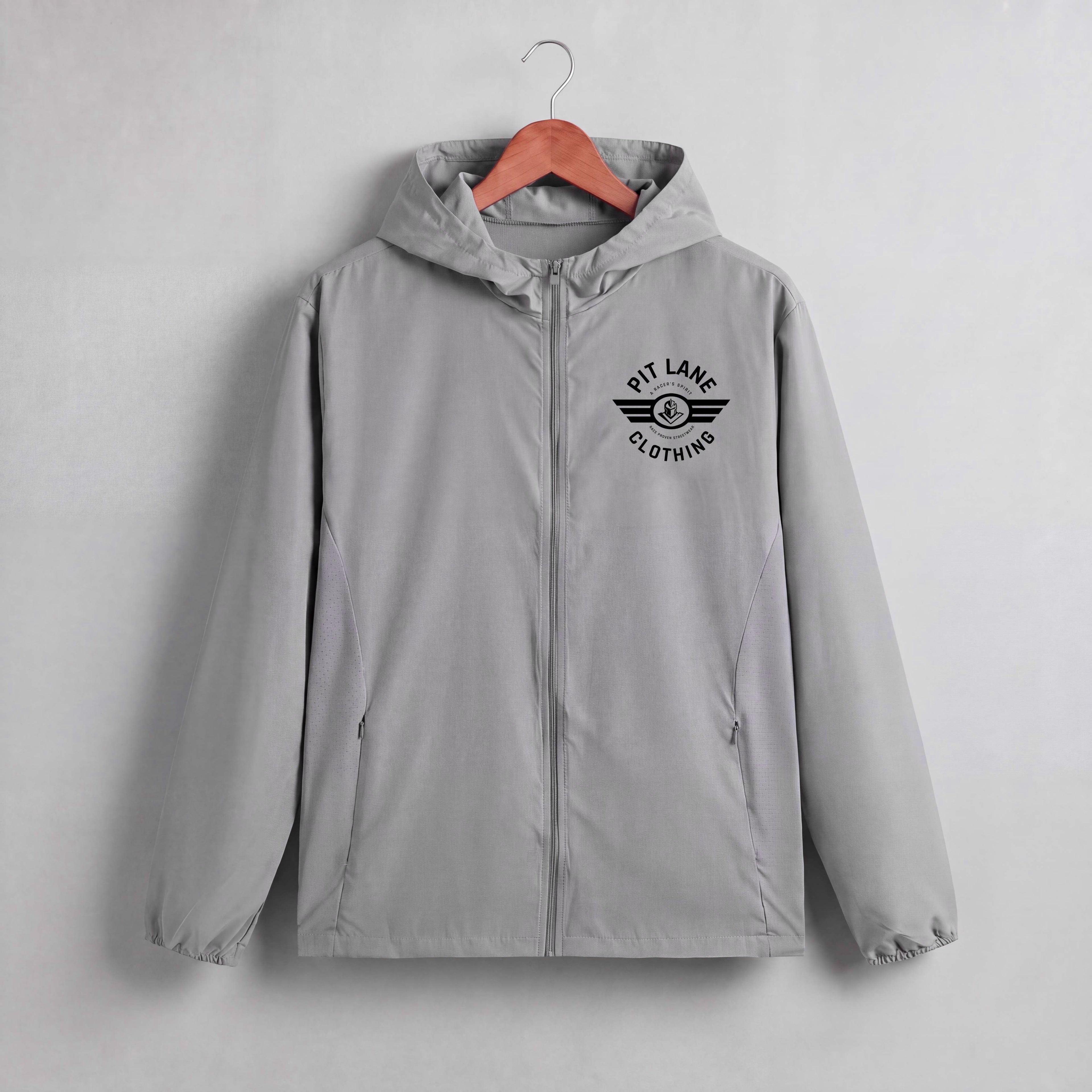 A light gray hooded zip-up jacket hanging on a wooden hanger against a light gray wall. The jacket features a black printed chest logo that reads 'PIT LANE CLOTHING' with wing details.