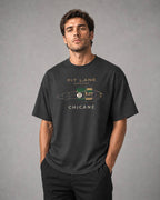 A man wearing a dark charcoal gray graphic t-shirt with a vintage race car design and the text 'PIT LANE CLOTHING' and 'CHICANE'.