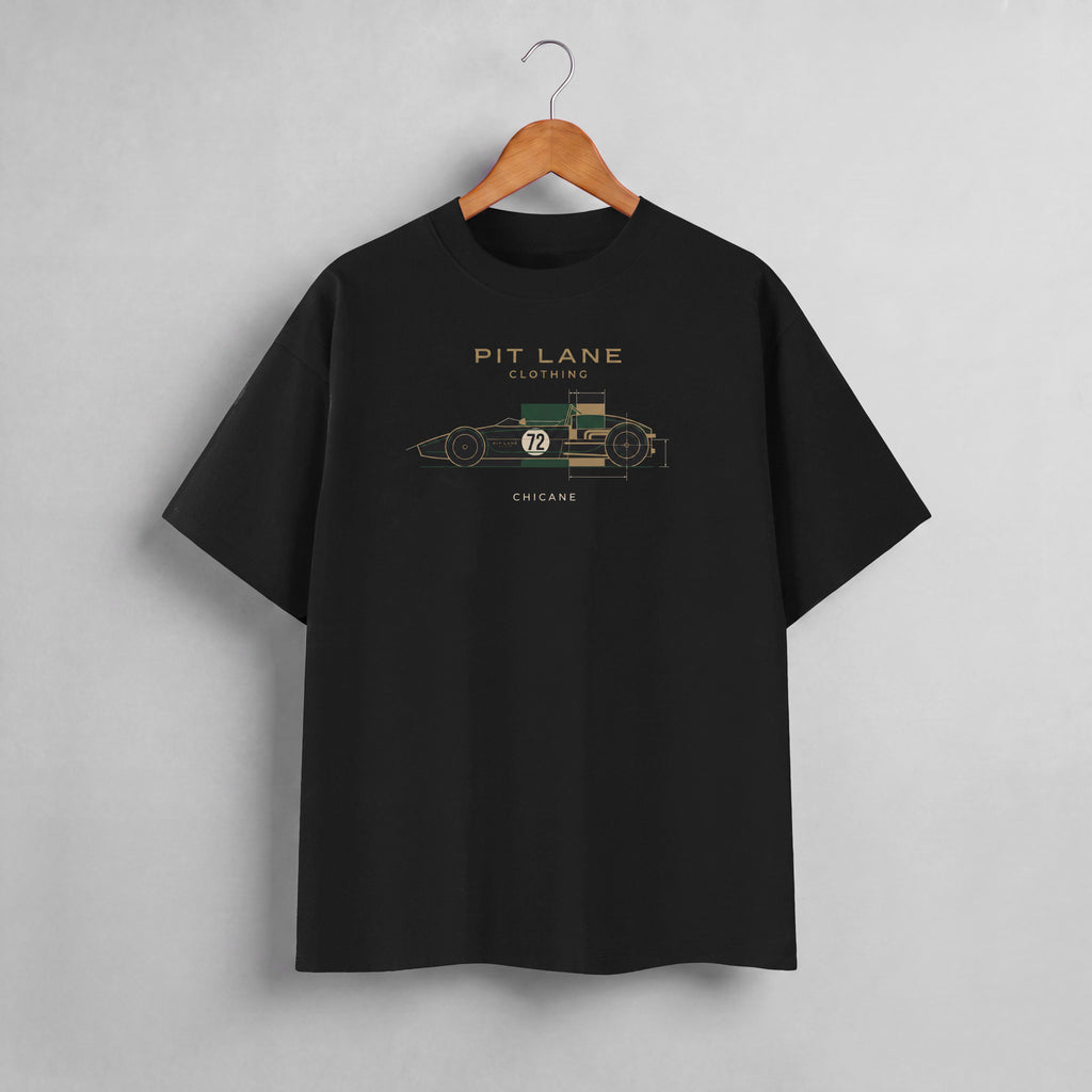 A black short-sleeve t-shirt hanging on a wooden hanger against a light gray wall. The shirt features a vintage-style race car graphic with the text 'PIT LANE CLOTHING' and 'CHICAGO' in gold and green.