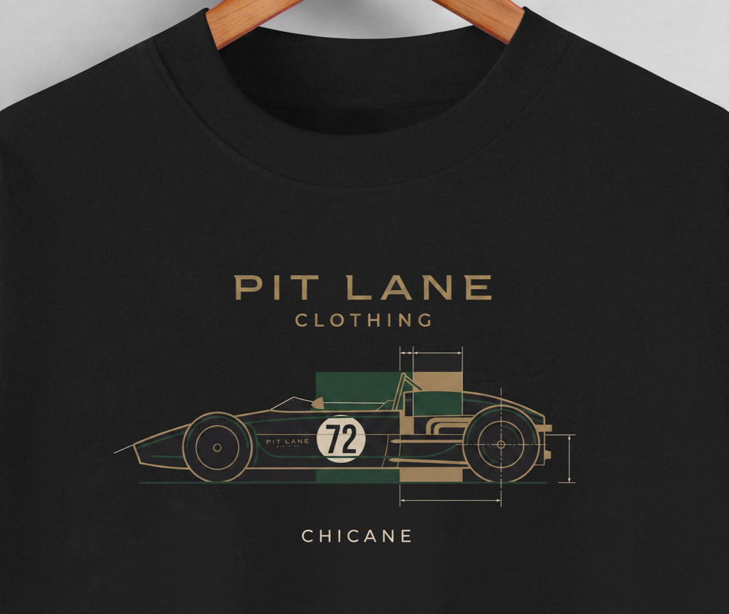 A close-up of a black crewneck t-shirt hanging on a wooden hanger, featuring a graphic of a vintage race car in green, beige, and white with the text 'PIT LANE CLOTHING' and 'CHICANE'.