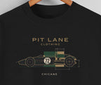 A close-up of a black crewneck t-shirt hanging on a wooden hanger, featuring a graphic of a vintage race car in green, beige, and white with the text 'PIT LANE CLOTHING' and 'CHICANE'.