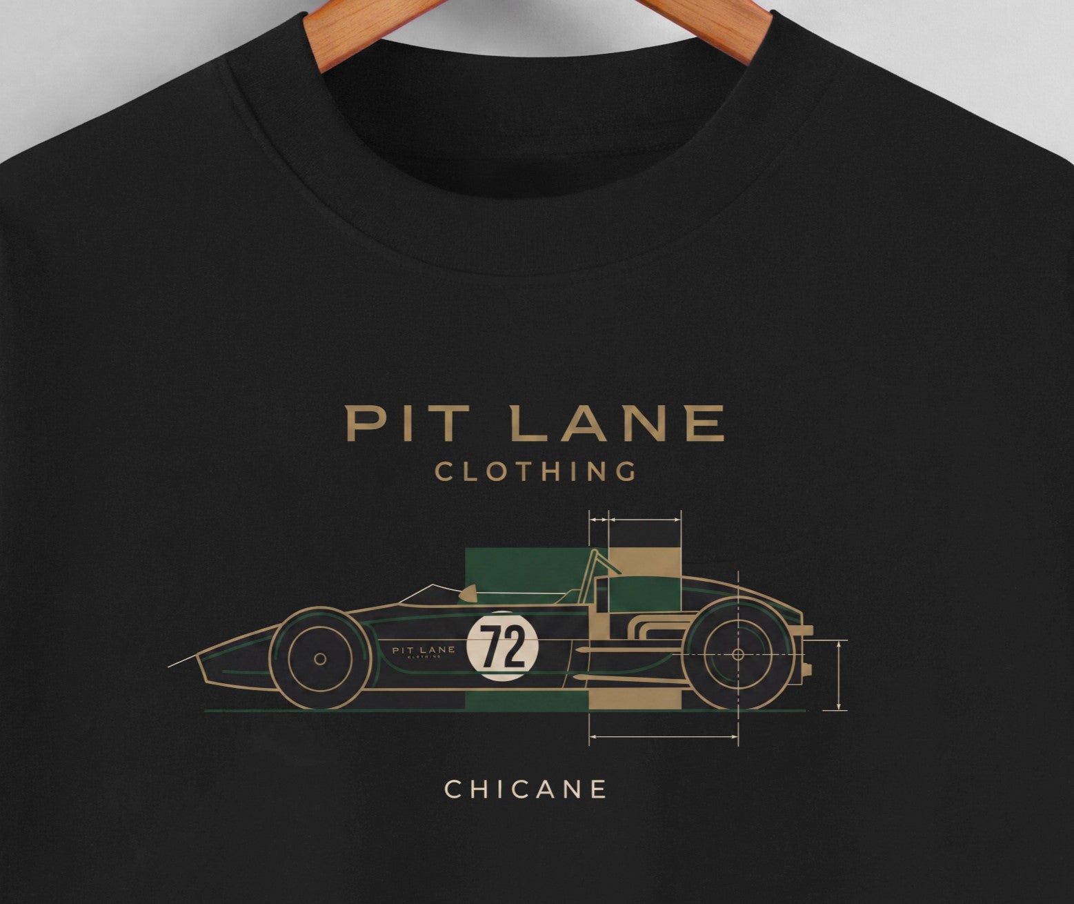 A close-up of a black crewneck t-shirt hanging on a wooden hanger, featuring a graphic of a vintage race car in green, beige, and white with the text 'PIT LANE CLOTHING' and 'CHICANE'.