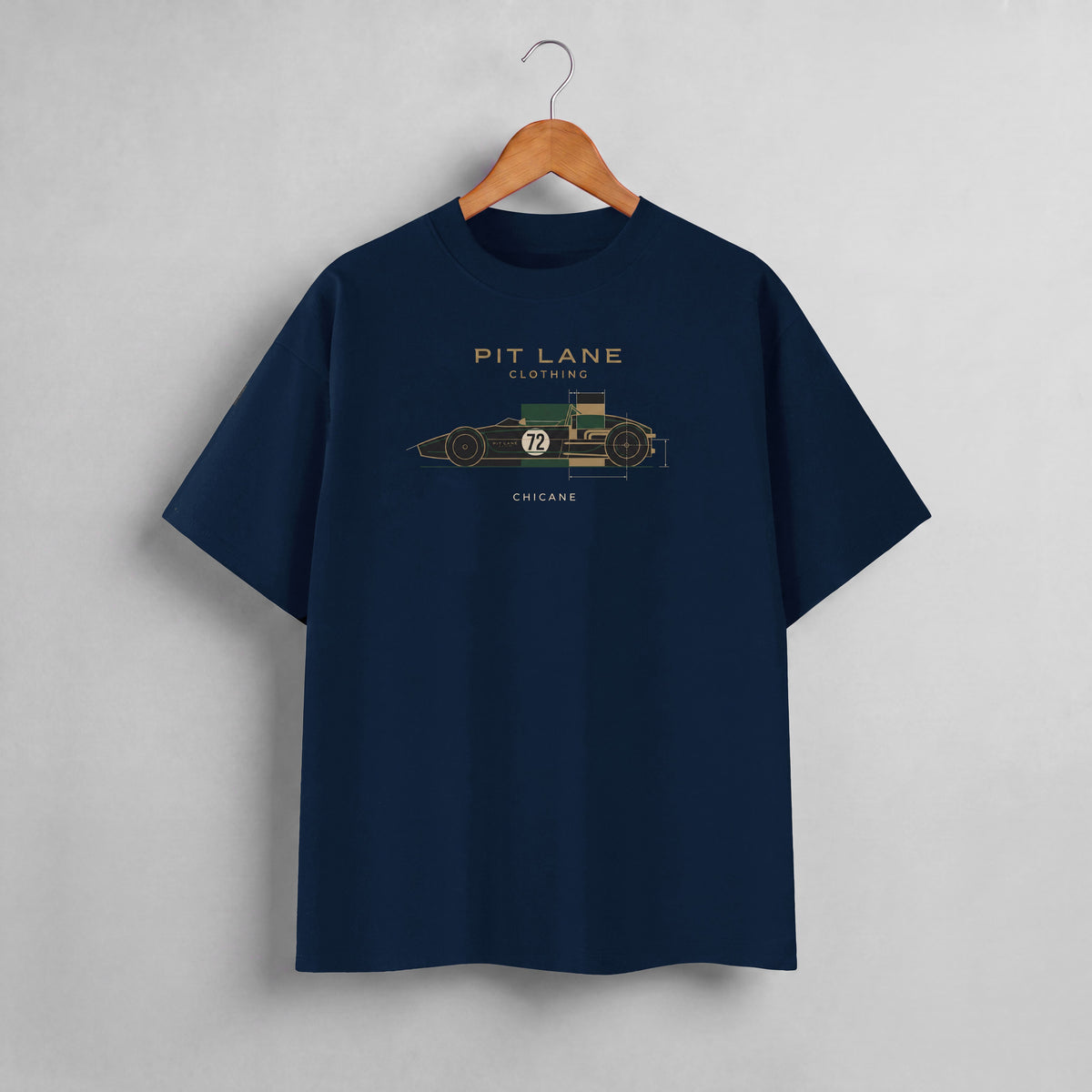A navy blue crewneck t-shirt hanging on a wooden hanger against a light gray wall. The shirt features a graphic of a vintage race car with dimensions and the text 'PIT LANE CLOTHING', 'CHICANE', and the number '72' in gold, green, and white.