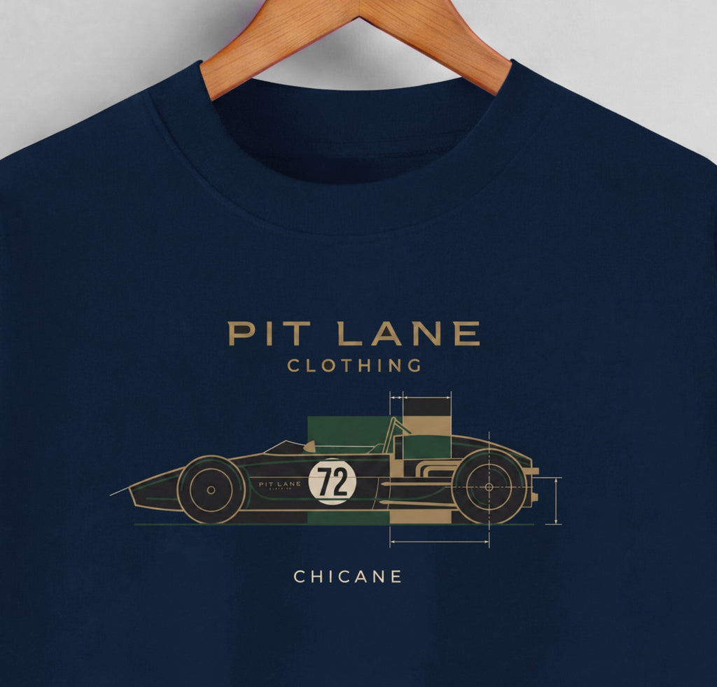 A navy blue crewneck t-shirt hanging on a wooden hanger against a light gray wall. The shirt features a graphic of a vintage race car with dimensions and the text 'PIT LANE CLOTHING', 'CHICANE', and the number '72' in gold, green, and white.
