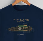 A navy blue crewneck t-shirt hanging on a wooden hanger against a light gray wall. The shirt features a graphic of a vintage race car with dimensions and the text 'PIT LANE CLOTHING', 'CHICANE', and the number '72' in gold, green, and white.