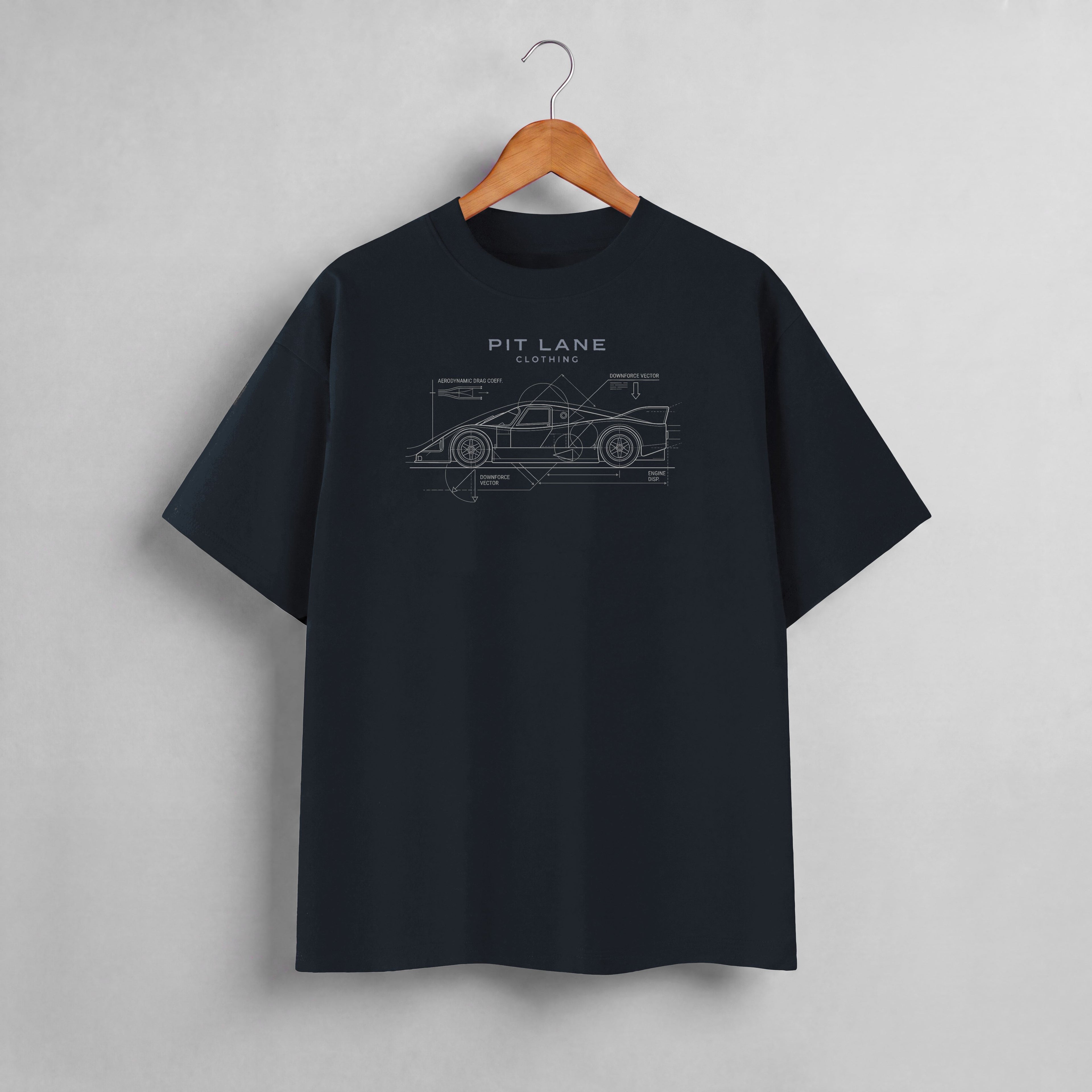 A dark navy blue crewneck t-shirt hanging on a wooden hanger against a light gray wall. The shirt features a white line-art graphic of a sports car with technical blueprint annotations and the text 'PIT LANE CLOTHING' printed on the chest.