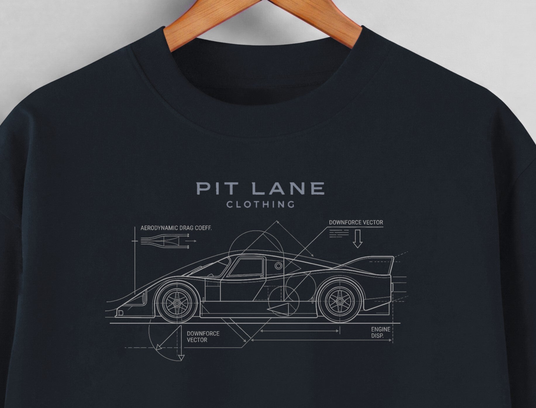 A dark navy blue crewneck t-shirt hanging on a wooden hanger against a light gray wall. The shirt features a white line-art graphic of a sports car with technical blueprint annotations and the text 'PIT LANE CLOTHING' printed on the chest.