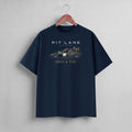 A navy blue short-sleeve t-shirt hanging on a wooden hanger against a light gray wall. The shirt features a graphic print of a race car and the text 'PIT LANE LEGENDS' and 'HEEL & TOE' in white and gold.