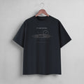 A black short-sleeve t-shirt hanging on a wooden hanger against a light gray wall. The shirt features a white line-art graphic of a race car with a clock and the text 'PIT LANE CLOTHING' printed on the chest.