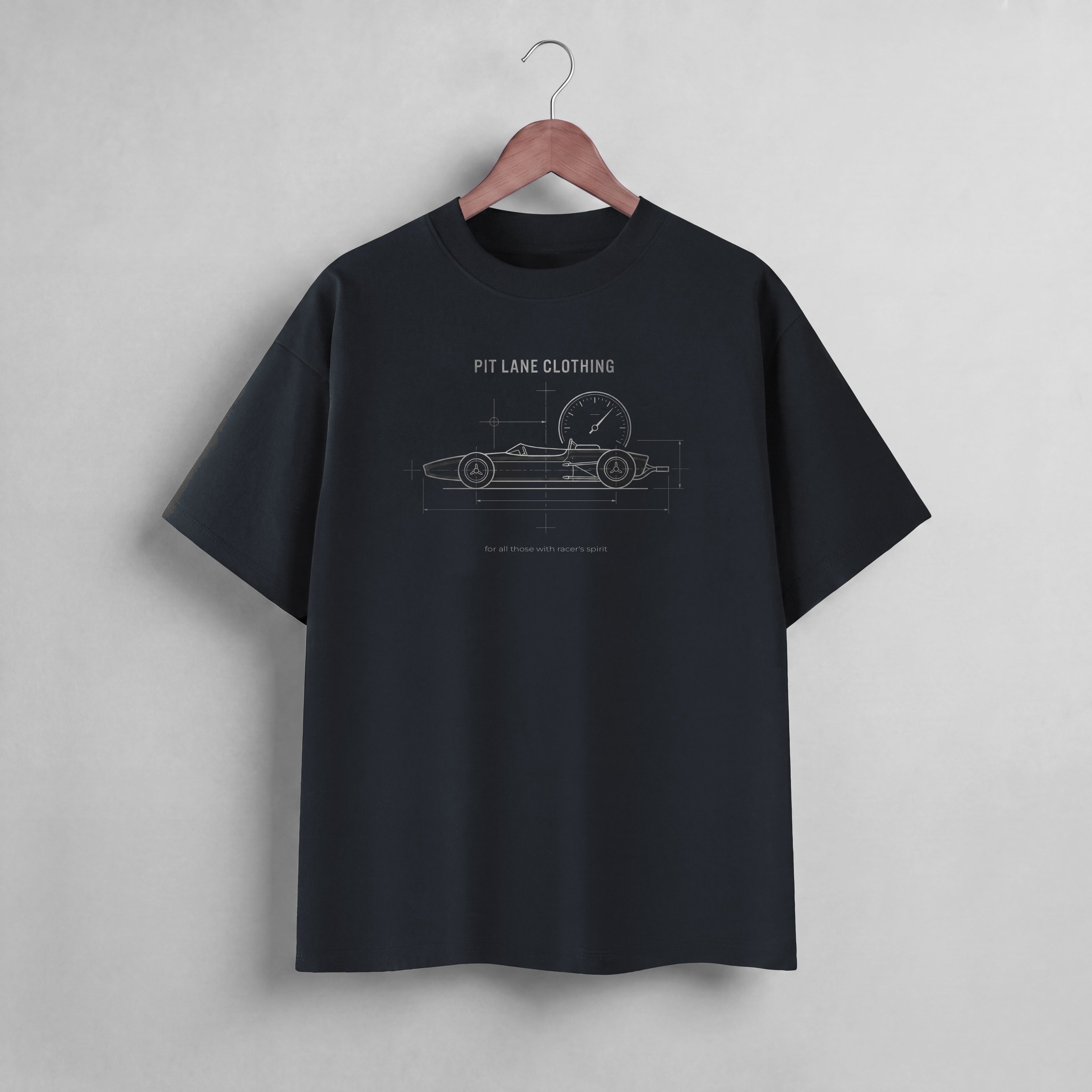 A black short-sleeve t-shirt hanging on a wooden hanger against a light gray wall. The shirt features a white line-art graphic of a race car with a clock and the text 'PIT LANE CLOTHING' printed on the chest.
