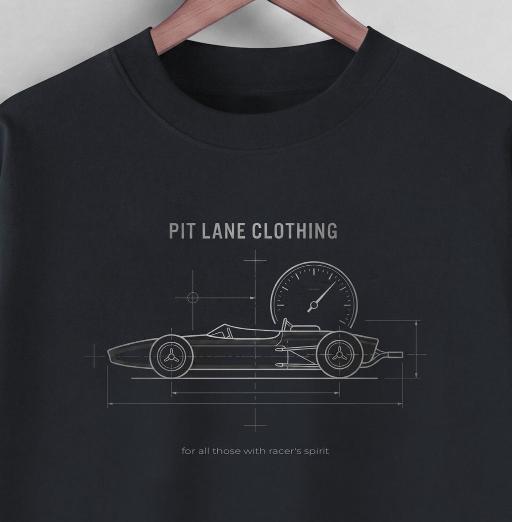 A black crewneck t-shirt hanging on a wooden hanger against a light gray wall. The shirt features a white blueprint-style graphic of a vintage race car with a speedometer, labeled 'PIT LANE CLOTHING' and 'for all those with racer's spirit'.