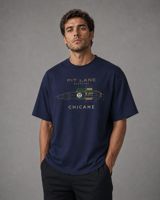 A man wearing a navy blue graphic t-shirt with a vintage race car design and the text 'PIT LANE CLOTHING' and 'CHICANE'.