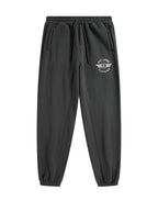 Black jogger pants with an elastic waistband, drawstring, side pockets, and a white circular winged logo on the left thigh that reads 'PIT LANE CLOTHING'.