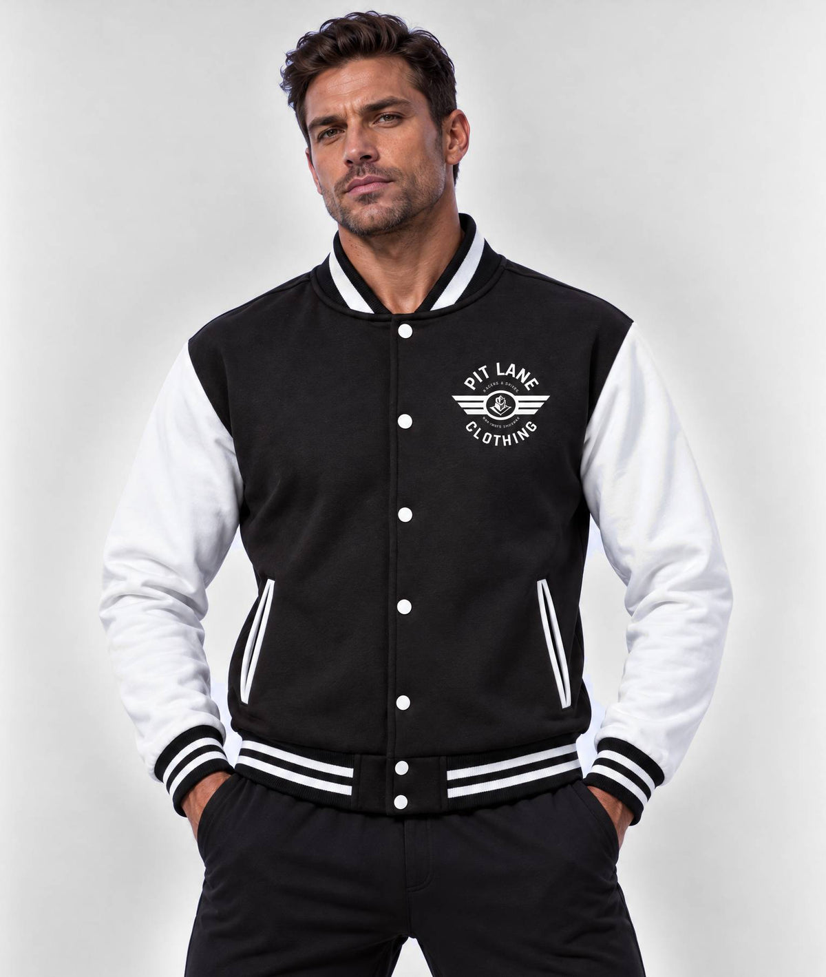 A man wearing a black and white varsity jacket with 'Pit Lane Clothing' logo on the chest, posed against a light gray studio background.