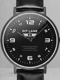 A Pit Lane Clothing analog wristwatch with a black leather strap, black dial, and silver-tone case, centered against a light gray textured background.