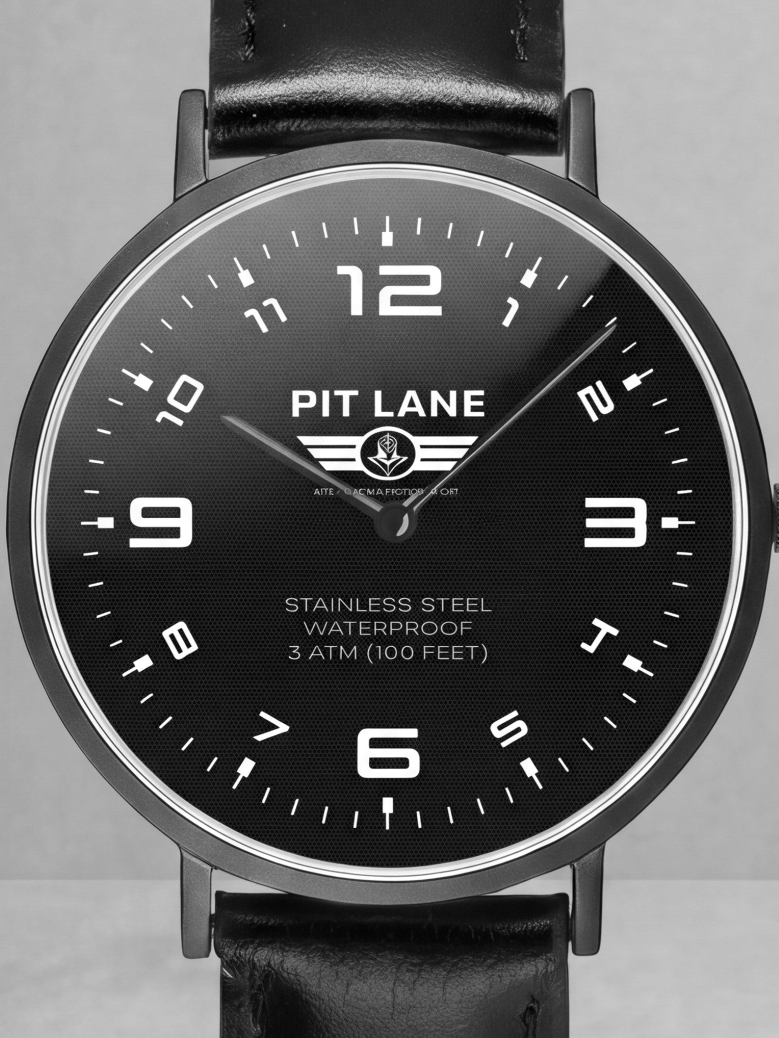 A Pit Lane Clothing analog wristwatch with a black leather strap, black dial, and silver-tone case, centered against a light gray textured background.