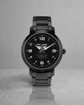 A black Pit Lane Clothing stainless steel watch with a matching black metal link bracelet, featuring a black dial with white Arabic numerals and hands, set against a neutral gray background.