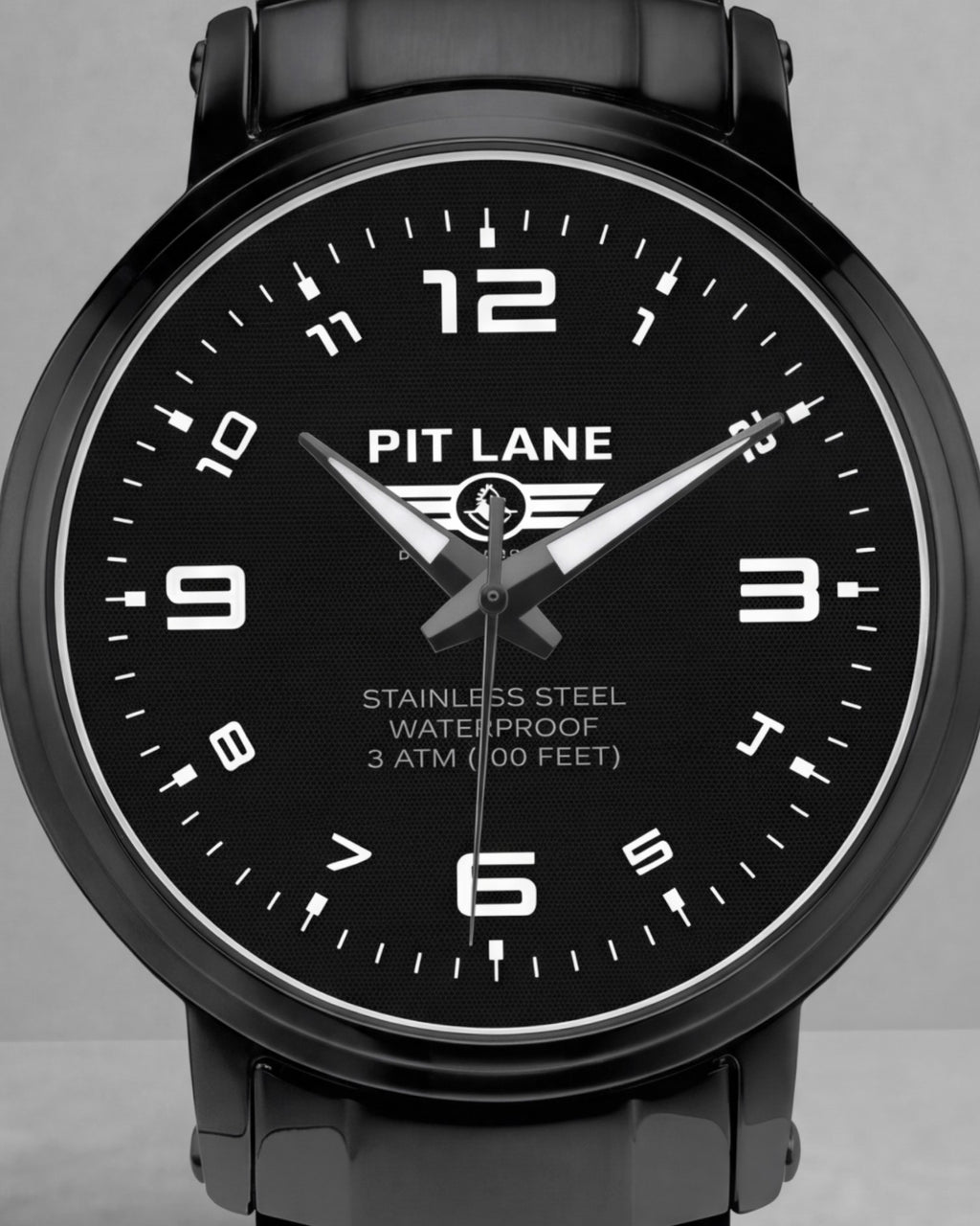 A black Pit Lane Clothing stainless steel watch with a matching black metal link bracelet, featuring a black dial with white Arabic numerals and hands, set against a neutral gray background.