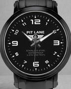 A black Pit Lane Clothing stainless steel watch with a matching black metal link bracelet, featuring a black dial with white Arabic numerals and hands, set against a neutral gray background.
