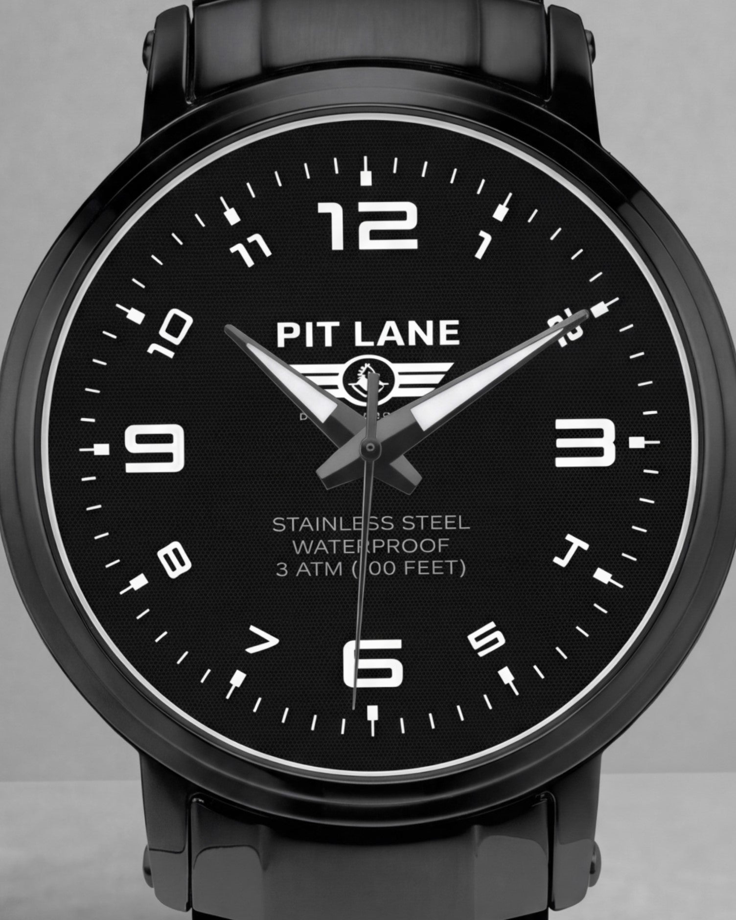 A black Pit Lane Clothing stainless steel watch with a matching black metal link bracelet, featuring a black dial with white Arabic numerals and hands, set against a neutral gray background.