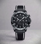A Pitlane chronograph watch with a black dial, black bezel, and a black rubber strap with white stripes, set against a neutral gray background.