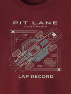 A close-up of a dark red crewneck t-shirt featuring a white blueprint-style graphic of a race car with technical annotations and the text 'PIT LANE CLOTHING' and 'LAP RECORD'.