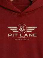 A close-up of a maroon hooded sweatshirt featuring a distressed cream graphic on the chest with the text 'PIT LANE' and 'RACE PROVEN' beneath a winged emblem.
