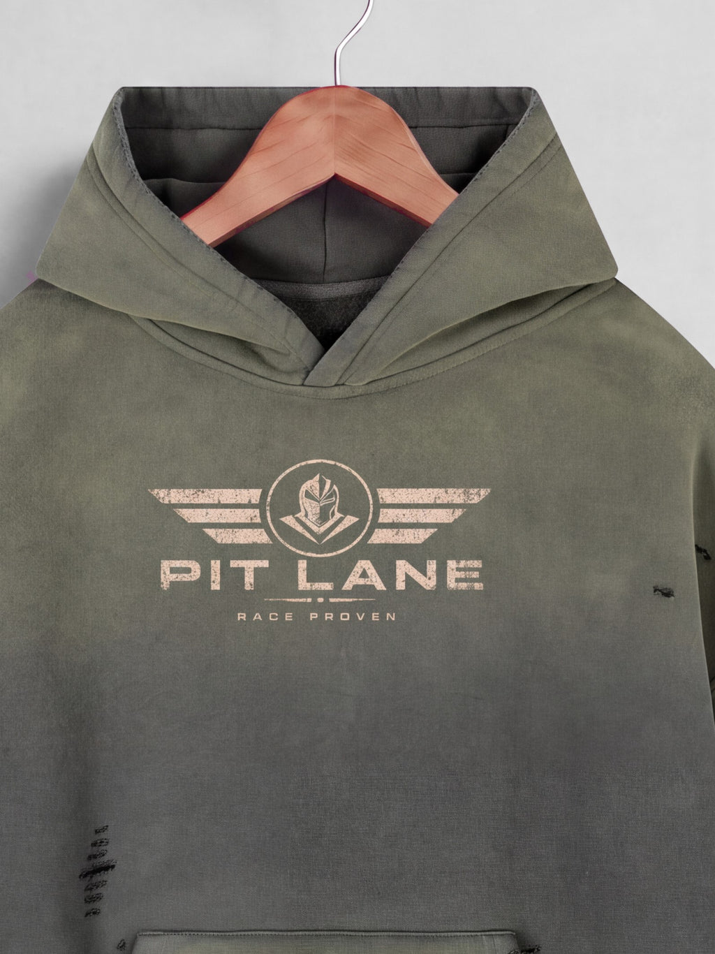 An olive green hooded sweatshirt with a distressed beige 'PIT LANE' winged logo on the chest, hanging on a wooden hanger against a light gray background.
