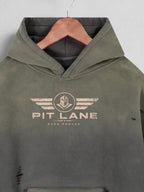 An olive green hooded sweatshirt with a distressed beige 'PIT LANE' winged logo on the chest, hanging on a wooden hanger against a light gray background.