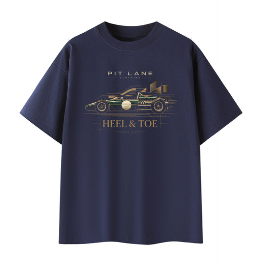 A navy blue short-sleeve t-shirt with a graphic print of a race car and the text 'PIT LANE CLOTHING' and 'HEEL & TOE' in gold and white, displayed on a solid white background.