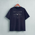 A black short-sleeve t-shirt hanging on a wooden hanger against a light gray wall. The shirt features a vintage-style race car graphic with the text 'PIT LANE CLOTHING' 