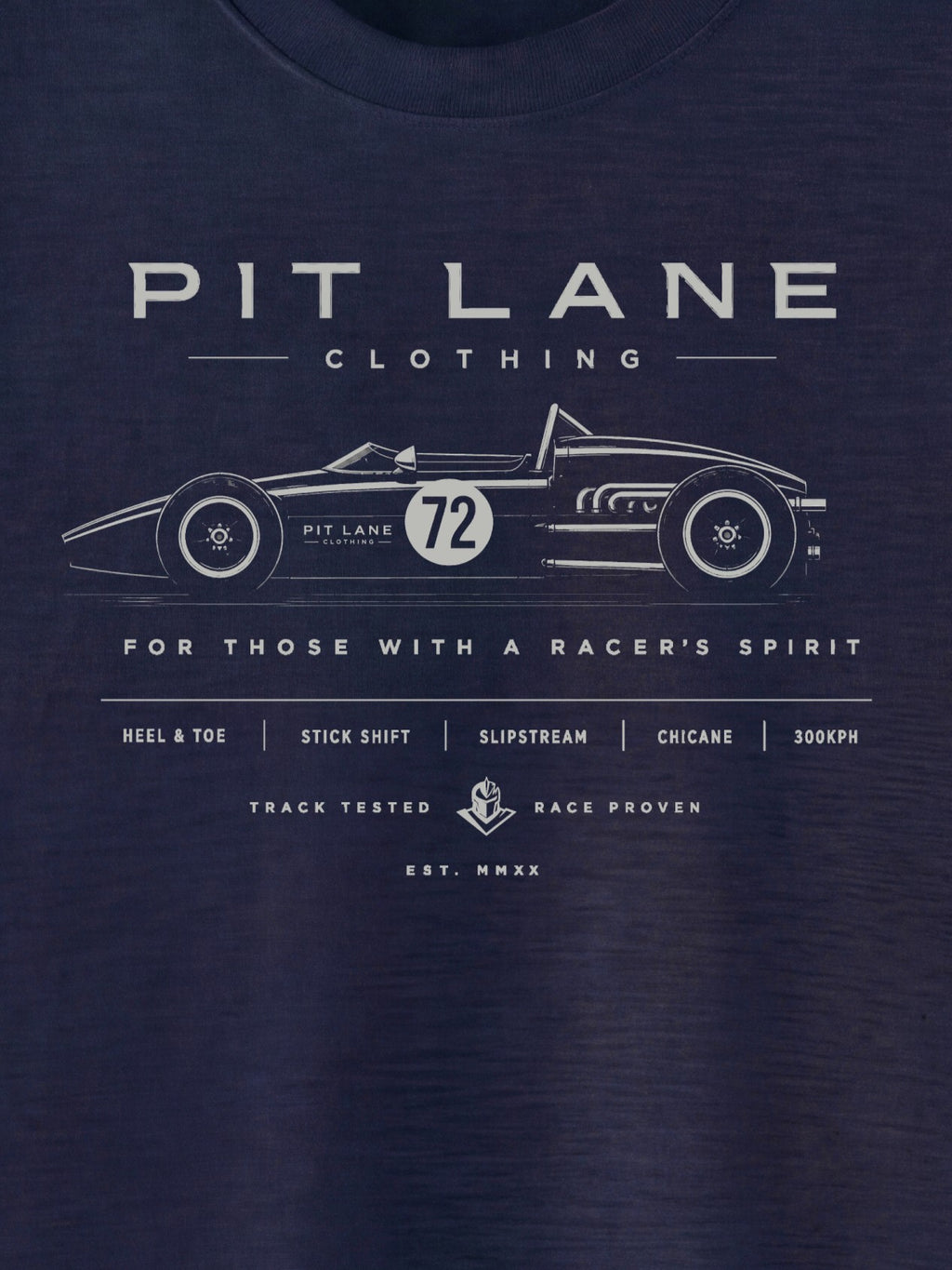 A close-up of a navy blue t-shirt featuring a white graphic print of a vintage race car and the text 'PIT LANE CLOTHING' and 'FOR THOSE WITH A RACER'S SPIRIT'.