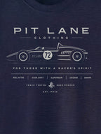 A close-up of a navy blue t-shirt featuring a white graphic print of a vintage race car and the text 'PIT LANE CLOTHING' and 'FOR THOSE WITH A RACER'S SPIRIT'.