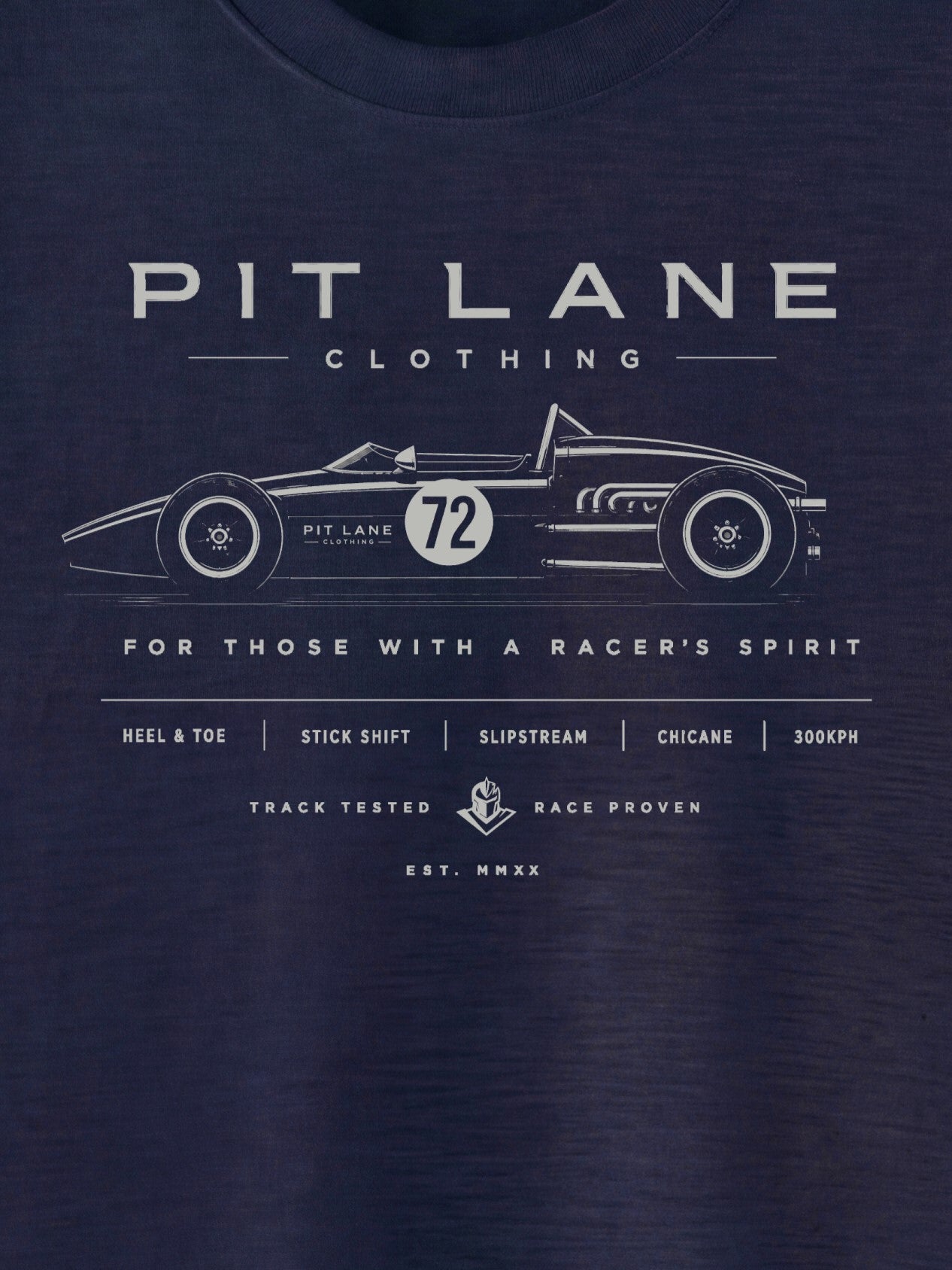 A close-up of a navy blue t-shirt featuring a white graphic print of a vintage race car and the text 'PIT LANE CLOTHING' and 'FOR THOSE WITH A RACER'S SPIRIT'.