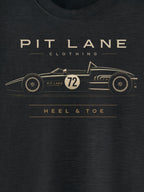 A close-up of a dark charcoal gray t-shirt featuring a gold graphic of a vintage race car with the text 'PIT LANE CLOTHING' and 'HEEL & TOE' printed on the front.