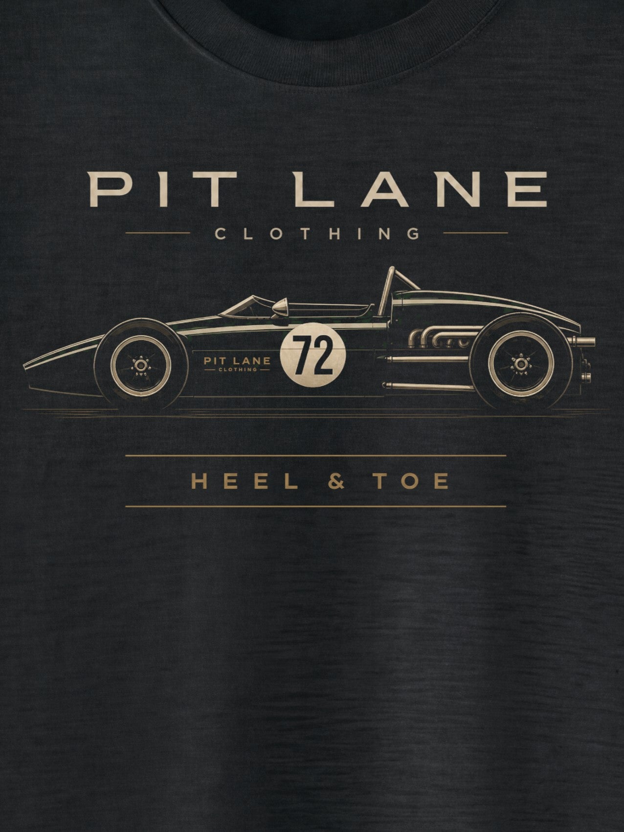 A close-up of a dark charcoal gray t-shirt featuring a gold graphic of a vintage race car with the text 'PIT LANE CLOTHING' and 'HEEL & TOE' printed on the front.