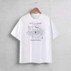A white short-sleeve crewneck t-shirt hanging on a wooden hanger against a light gray wall. The shirt features a black graphic print of a circular mechanical design resembling a sci-fi helmet or engine schematic, with the text 'PIT LANE CLOTHING' above and 'DOWNFORCE' below.