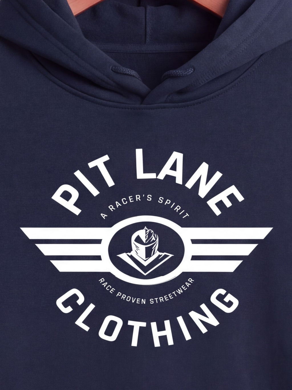 Close-up of a navy blue hoodie featuring a large white graphic print on the chest that reads 'PIT LANE CLOTHING' with a central emblem and wing-like stripes.