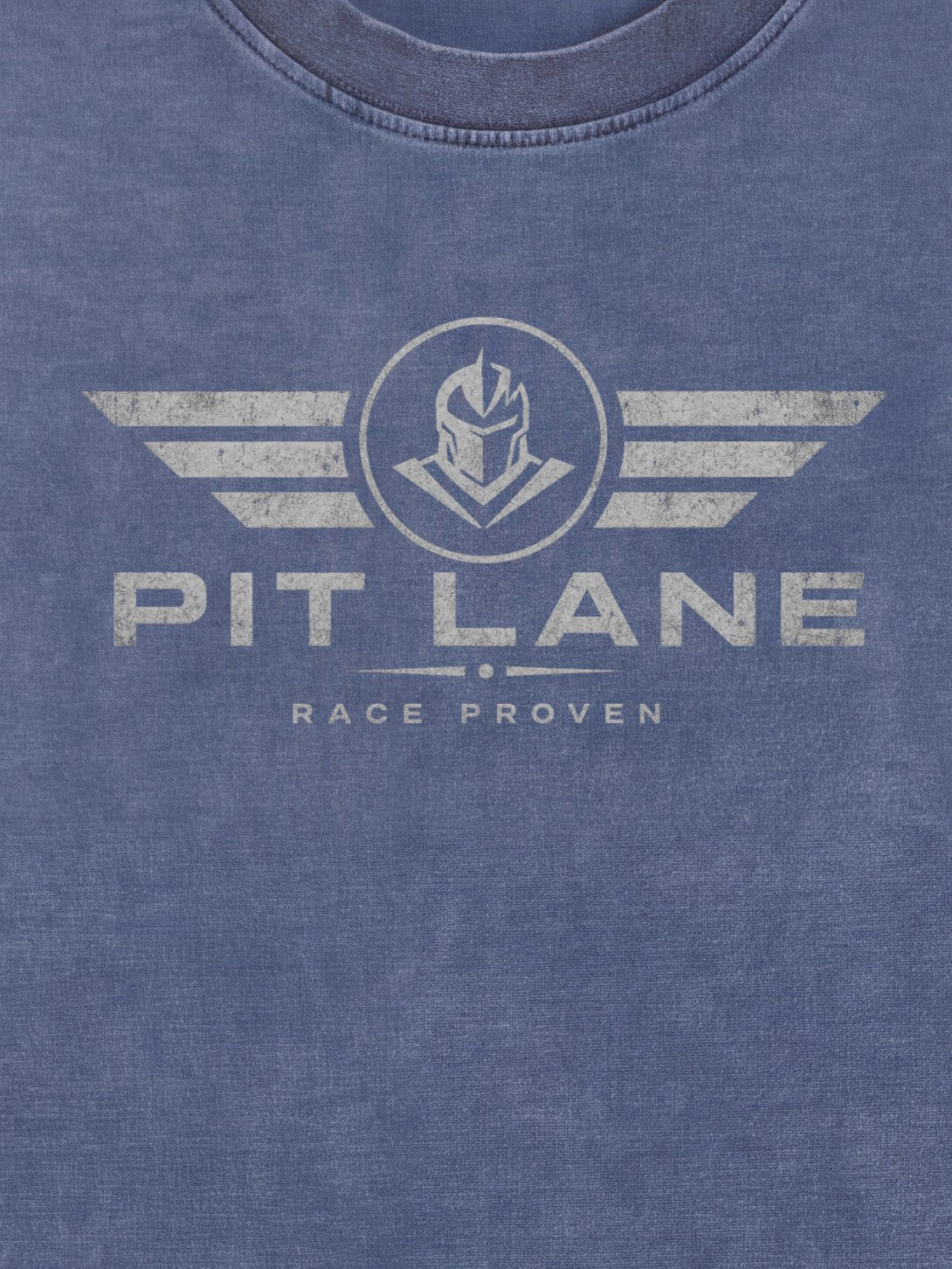 Close-up of a heathered blue crewneck t-shirt featuring a distressed white graphic print of a helmeted knight inside a circle with wings, and the text 'PIT LANE' and 'RACE PROVEN'.