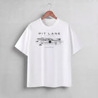 A white short-sleeve crewneck t-shirt hanging on a wooden hanger against a light gray wall. The shirt features a black graphic print of a race car with the text 'PIT LANE CLOTHING' and 'SLIPSTREAM' on the chest.